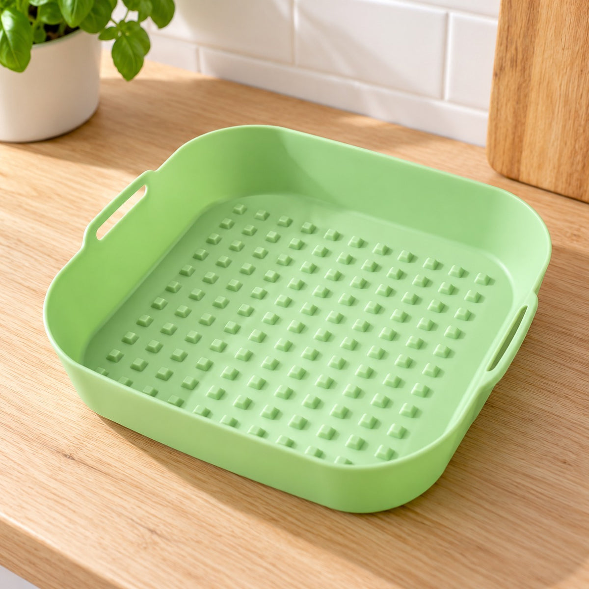 Groen siliconen airfryer-bakje met noppen op de bodem en handvatten